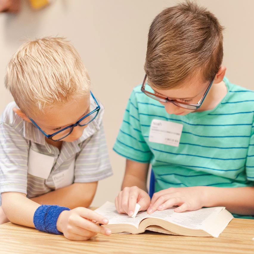 Two young kids read a bible together.